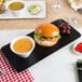 A rectangular matte black Acopa stoneware plate with a burger and soup on it.