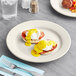 An Acopa ivory stoneware plate with eggs benedict and a fork on a table.