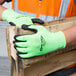 A person wearing Cordova Hi-Vis lime green gloves with black foam nitrile palms holding a piece of wood.