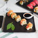 A close-up of Acopa matte black stoneware plates with sushi on a table.