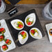 Acopa matte black stoneware plates with small bowls of food on a table.