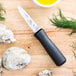 A Choice Boston Style Oyster Knife with a black handle next to oysters on a cutting board.
