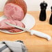 A Choice serrated utility knife with a white handle on a plate with sliced ham.