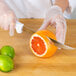 A person using a Choice serrated utility knife to cut an orange.