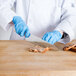 A person in a white coat and blue gloves using a Choice chef knife to cut meat.