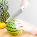 A person in gloves cutting a watermelon with a Choice chef knife.