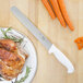 A Choice white straight edge slicing knife on a plate of food with turkey and carrots.