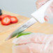 A person uses a Choice smooth edge paring knife with a white wide handle to cut a strawberry.
