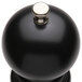 A black round pepper mill with a silver knob.