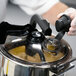 A gloved hand pouring liquid into a stainless steel bowl on a Hobart food processor.