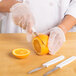 A person in white gloves using a Choice paring knife to slice an orange on a table.