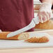 A person using a Choice bread knife to cut bread on a cutting board.