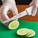 A person wearing a glove cutting a lime with a Choice serrated utility knife.