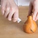 A person cutting a pear with a Choice serrated paring knife with a white handle.