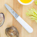 A Choice stainless steel clam knife on a cutting board with a clam shell