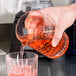 A hand pouring a clear cocktail into a Libbey Carats cocktail stirring glass on a counter.
