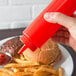 A hand holding a Choice red squeeze bottle over a burger and fries.