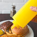 A hand holding a yellow Choice squeeze bottle over a plate of food.