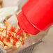 A red Choice wide mouth squeeze bottle pouring ketchup onto french fries.