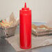 A red Choice wide mouth squeeze bottle filled with ketchup on a table with french fries.