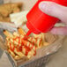 A hand pouring ketchup from a red Choice squeeze bottle onto a basket of french fries.