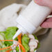 A close-up of a hand holding a Choice clear squeeze bottle of white sauce over a salad.