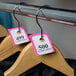 A rack of clothes with Choice Pink paper coat check tags on them.
