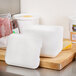 A white foam container with a square top filled with white foam cubes on a cutting board next to cheese and meat.