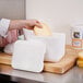 A hand using a knife to put cheese into a white Nordic insulated foam container.