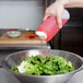 A hand using a Tablecraft clear squeeze bottle to pour pink liquid onto a bowl of salad