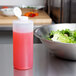 A bowl of salad with lettuce, tomatoes, and other vegetables next to a Tablecraft clear squeeze bottle with pink liquid in it.
