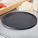 A black Matfer Bourgeat carbon steel pizza pan on a metal surface.