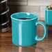 A turquoise Fiesta china mug with a handle filled with coffee on a table.