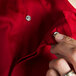 A person's fingers buttoning a Chef Revival tomato red chef jacket.