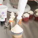 A person using an Ateco pastry bag to frost a cupcake with white frosting.