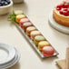 A row of colorful macarons on an Acopa rectangular stainless steel tray with a bowl of blueberries.