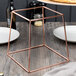 An Acopa rose gold metal display stand on a table with a glass jar on it.