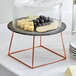 An Acopa rose gold metal display stand with food on a plate.