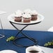 An Acopa black metal display stand holding a plate of cupcakes on a table.