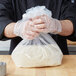 A person in a chef's uniform holding a plastic bag of rice.