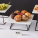 A tray of muffins and grapes on an Acopa black metal display stand.
