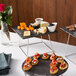 A table with a stainless steel Acopa display stand holding appetizers, cheese, and a bowl of blackberries.