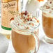 A glass mug of brown liquid with whipped cream and nuts.