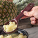 A person holding a Carlisle Measure Misers portion spoon filled with pineapple.
