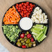 A Fineline black plastic 7-compartment tray with carrots, tomatoes, broccoli, and olives with a bowl of dip.