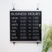 A black and white Headline Sign business hours sign on a wall.