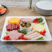 A white Fineline square plastic catering tray with meat, cheese, and olives on a table.