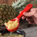 A hand uses a red Carlisle Measure Misers portion spoon to serve pineapple into a bowl.
