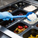 A person in blue gloves using a Carlisle blue acetal portion spoon to serve food from a black container.