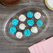 A Fineline clear plastic oval catering tray with a plate of cupcakes with blue and white frosting and sprinkles.